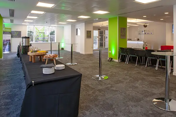 The foyer to Woburn House, a central London conference venue, with a table set with plates and pastries, standing tables and large open standing areas.